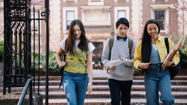 three students reading books and walking out of their university
